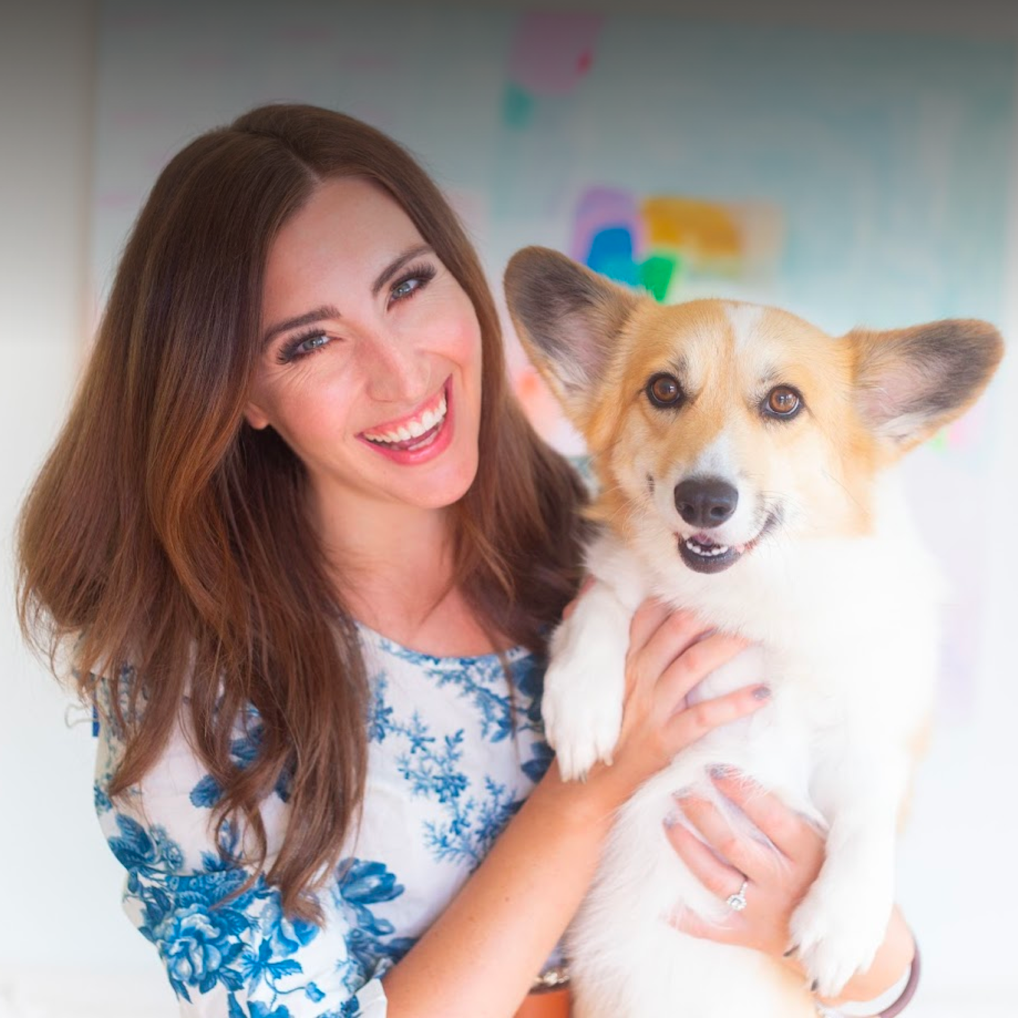 A smiling young woman poses with a corgi in her arms